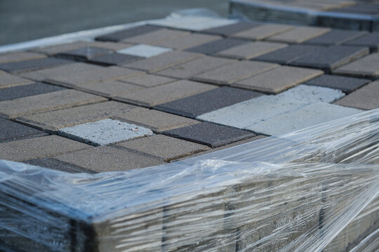 Tiles for road Construction are compiled for the construction of a pedestrian sidewalk. Packs of gray cement paving slabs are wrapped in plastic wrap in the warehouse. 