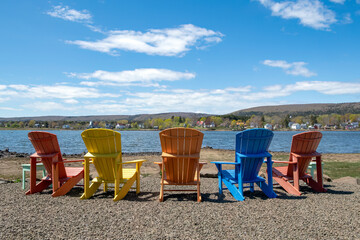 Colorful painted wood deck chairs on a gravel shore of a harbor on the east coast of Canada.