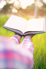 Happy woman lying on green grass reading a book in the park (outdoors) SSTKHome