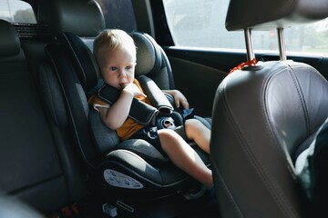 Child toddler boy sitting thoughtfully in a car in the back seat in a child car seat