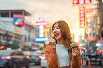 Happy young tourist Asian woman enjoy and fun traditional asian street food at Bangkok Chinatown, Female shopping and eating street food on summer holiday vacation.