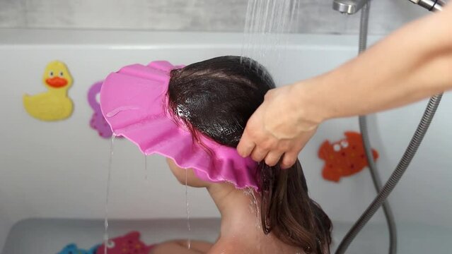 Mom washes the head of a little girl in the bathroom. Mom is bathing the baby in slow motion. Care of children. Water treatments and health care