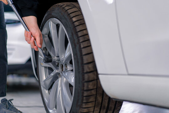 Auto mechanic man changing a wheel on a luxury white car using a balloon wrench at a car service station close-up