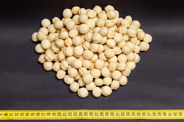 wheat, heap of round wheat snacks next to measuring tape, black background, generated with extruder machine