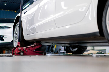 White luxury car being lifted with a red wheel change jack at a car service during detailing and dry cleaning