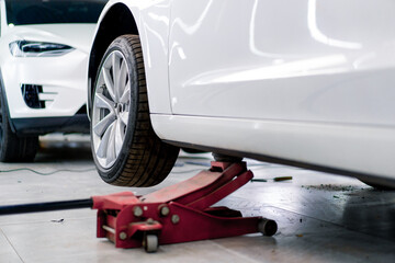 White luxury car being lifted with a red wheel change jack at a car service during detailing and...