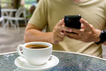  A cup of coffee with man using smart phone sitting in a coffee shop terrace background.