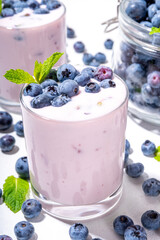 Blueberry yogurt, smoothie or milkshake on portioned glasses with fresh blueberries decor on it, and a lot of fresh berries on white kitchen table background copy space