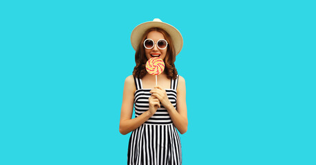 Portrait of happy young woman with colorful lollipop wearing summer straw hat, sunglasses, striped...