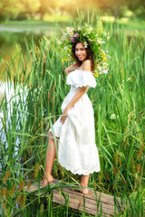 Young beautiful woman in a white dress and a wreath of wild flowers on Ivan Kupala near the water