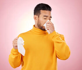 Sick, tissues and man blowing his nose in a studio with a cold, flu or sinus allergies. Illness, hayfever and Indian male person with paper napkin for virus or infection symptoms by a pink background