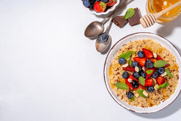 Summer breakfast oatmeal with strawberry, blueberry, nuts, chocolate and honey top view copy space, traditional summer fruit and berry oats porridge