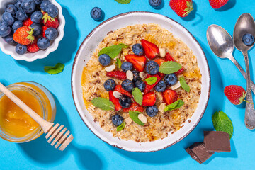 Summer breakfast oatmeal with strawberry, blueberry, nuts, chocolate and honey top view copy space, traditional summer fruit and berry oats porridge