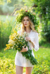 Portrait of a blonde woman with wild flowers on a background of nature in the summer at sunset. A girl in a wreath and a white shirt on the feast of Ivan Kupala. Soft golden color