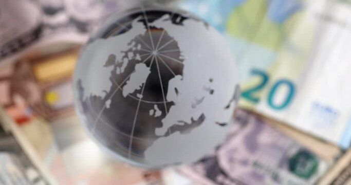 Transparent glass ball stands on banknotes of different countries. World economy concept