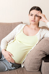 Young pregnant woman with headache sitting on sofa. Pregnancy expectation concept
