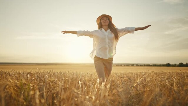 Romantic carefree happy woman running on yellow wheat field with spreading flying arms enjoying freedom calmness on rural nature during vacations holidays. Rest, relax in country, village at sunset.