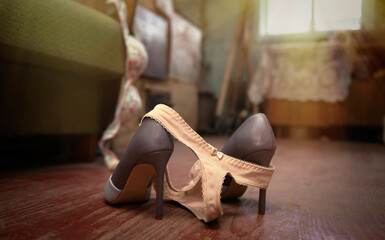 Female sexy underwear thrown on the floor with a high heeled shoes on a village floor near the bed....