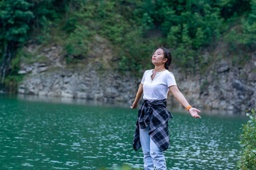 a young woman stands by the lake with closed eyes and outstretched arms, breathing deeply and enjoying the fresh air