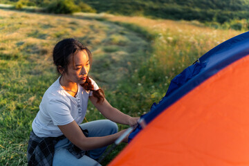 a young woman sets up a tent in a meadow after a hike, she is ready to rest