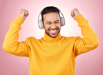 Music, headphones and man or winner success, yes and celebration for podcast, radio news and bonus. Motivation, power and happy person dance, listening to audio and excited on studio pink background