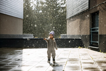 Child standing under the rain on a spring day, catching raindrops.