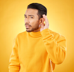 Whisper, gossip and asian man with hand on ear in studio for speak up body language on yellow...