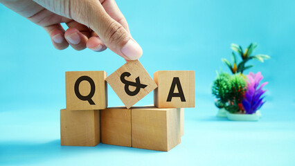 Hands holding wooden block with abbreviations Q and A on wooden block surface with engraved effect...