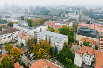 Beautiful foggy Vilnius city scene in autumn with orange and yellow foliage. Aerial early morning view.