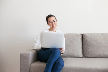 Young woman working on laptop. Millennial girl working remote job from home, sitting on the cozy sofa, smiling. 