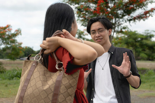 A young man tries to calm down his irate girlfriend from hitting him with her bag.