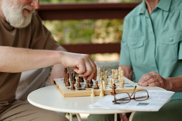 Fototapeta na wymiar Hands of senior man and woman sitting by small table with chess board and playing chess together while one of them making move