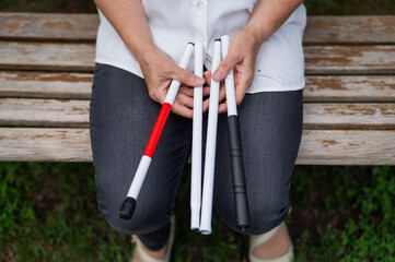 An elderly blind woman sits on a bench in the park. Close-up of female hands with folded tactile...