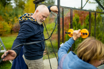 Senior couple working on a project in their garden. Man and woman constructing a greenhouse in...