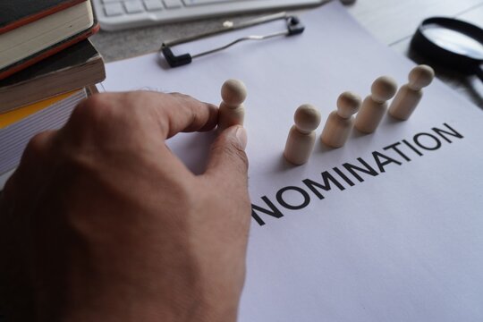 Hand pick wooden doll and text NOMINATION. Nominating a candidate for promotion. Select and designate an employee. Career advancement and social growth.
