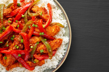 Homemade Simple Chili Chicken with White Rice on a Plate on a black background, top view. Flat lay, overhead, from above. Copy space.