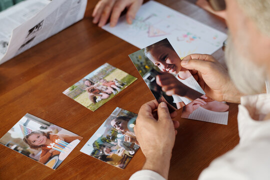 Focus on hands of grandfather holding picture of his cute granddaughter over wooden table with set of photos of other grandchildren