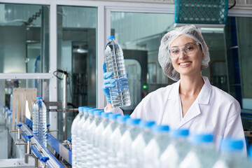 Caucasian women scientist with lab cote inspect quality of drinking water inside of the production line factory while using digital tablet to check cleanliness and standard, quality assurance