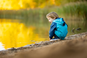 Adorable toddler boy having fun by the Gela lake on sunny fall day. Child exploring nature on autumn day in Vilnius, Lithuania.