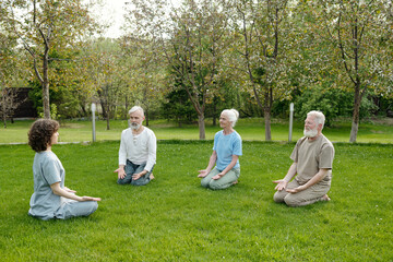 Three senior patients of retirement home repeating exercise after their instructor or caregiver...