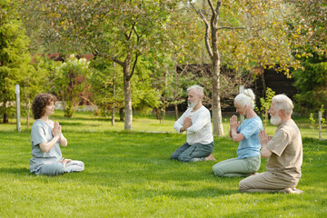 Side view of young female yoga instructor and group of senior patients of retirement home...