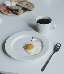 A light breakfast on a white table, a fried egg, and black coffee.