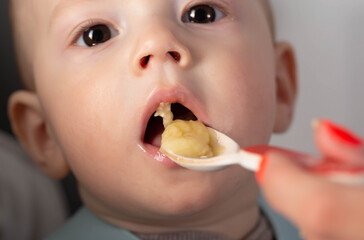 The first feeding with fruit puree for a baby boy who is 6 months old, close-up