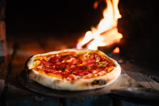 Placing italian pizza pepperoni in a wood-fired oven. Pizza with salami on pizza shovel in hot oven close up. Food photography