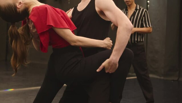 Medium slowmo of sensual Caucasian couple dancing tango while having individual dance class with Biracial male teacher in spacious ballroom