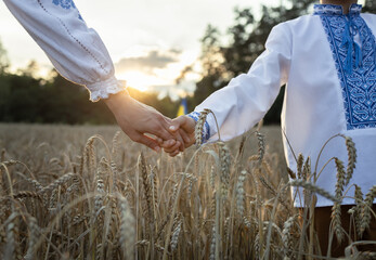 woman's hand in vyshyvanka holds child's hand in sunset backlight of the sun among the spikelets in a wheat field. Ukrainian family, unity, support, stand with Ukraine. Independence Day of Ukraine