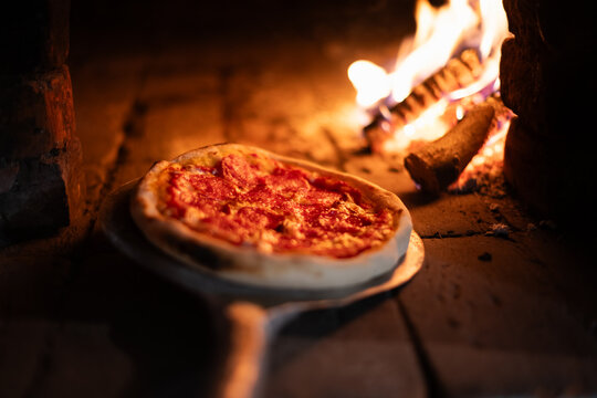 Italian pizza pepperoni is cooked in a wood-fired oven. Pizza with salami on pizza shovel in hot oven close up. Food photography