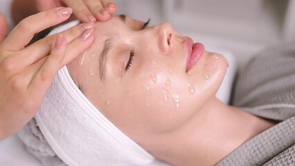 The cosmetologist applies a special gel, scrub, peeling to the face of a pretty caucasian woman to improve the quality of facial skin. Facial skin care procedures in a beauty salon. Beauty treatment - Powered by Adobe