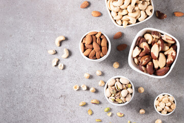 Large assortment of nuts in different bowls on stone table.
