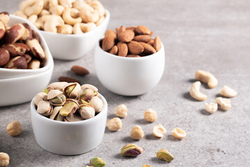 Large assortment of nuts in different bowls on stone table.